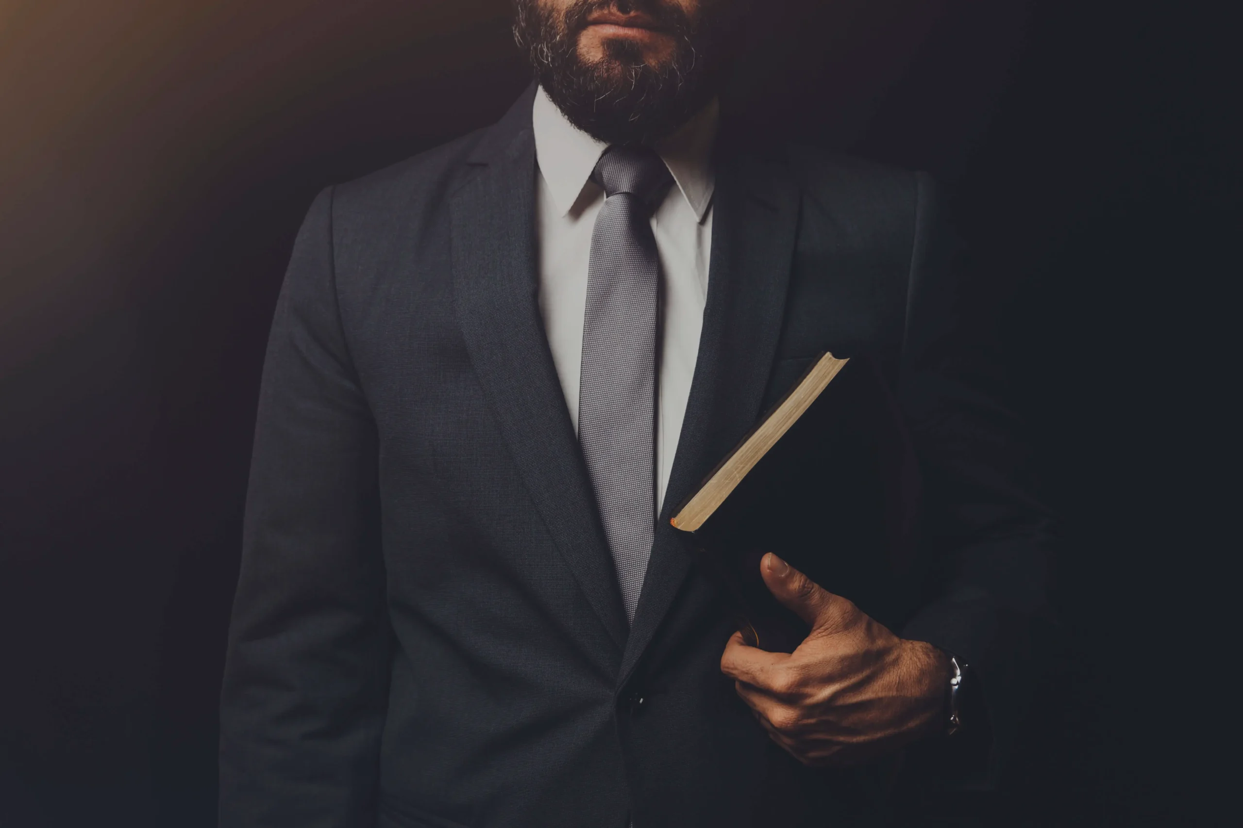 man in suit holding a bible in his arm on a black background