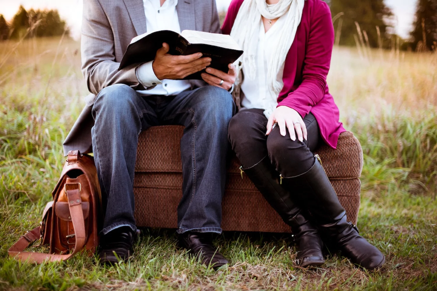 a pastor and his wife sit outside in a grassy field and read Scripture together during Pastor Appreciation Month