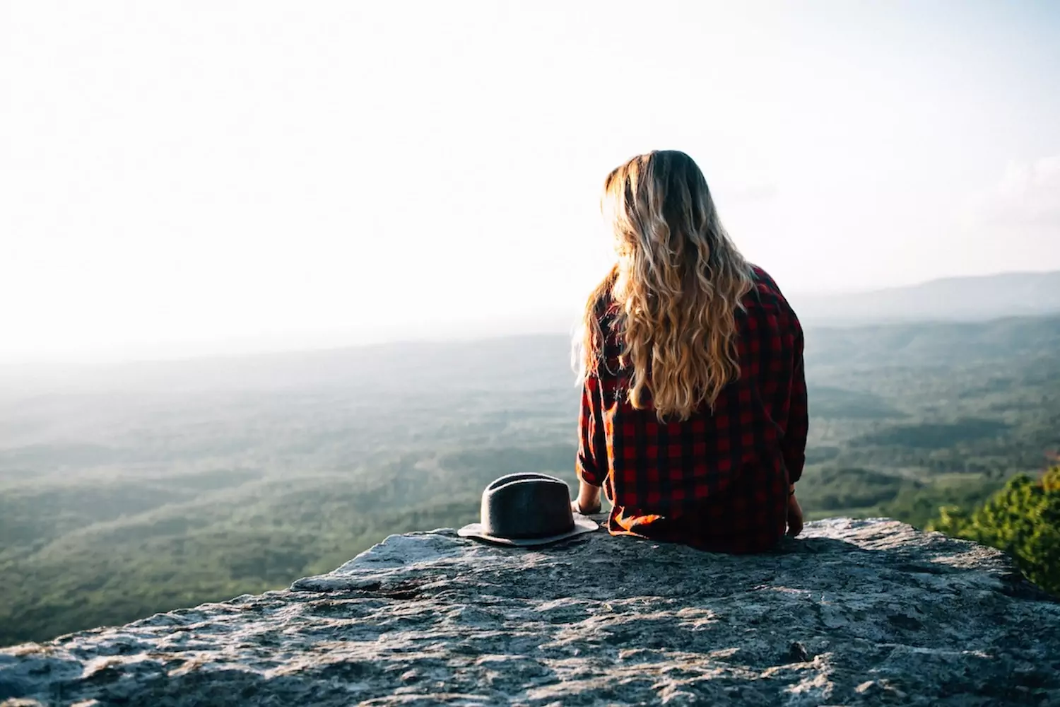 a pastor's wife sits on the edge of a cliff, overlooking treetops below