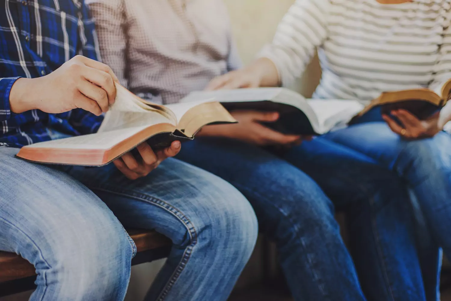 three Christians sit on a bench with their Bibles in their laps and study them together