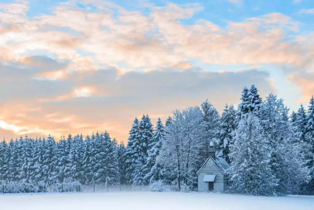 Small wooden chapel in snowbound frosty forest under morning sunrise sky. Amazing idyllic winter landscape in Bavarian rural region Allgaeu.