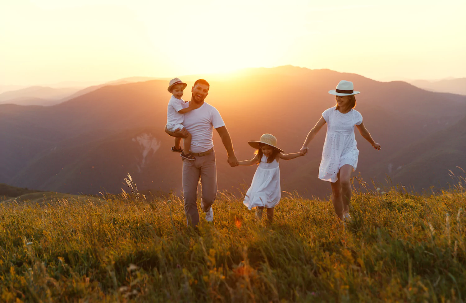 a pastor walks hand-in-hand with his wife and two children, understanding that this first ministry is to his family; they're wearing white outfits and strolling through a field at golden hour