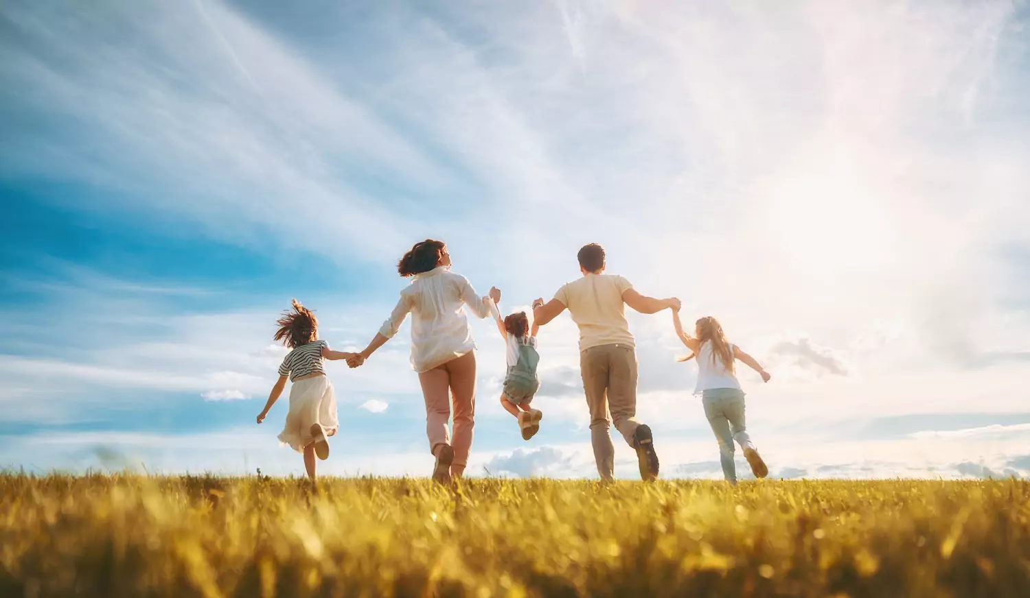 A pastor and his wife run through a golden field holding the hands of their three daughters.