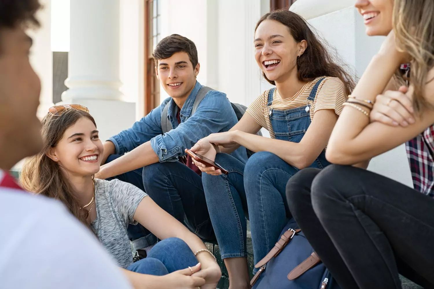 A group of youth group students sit together outside their church, talking and laughing.