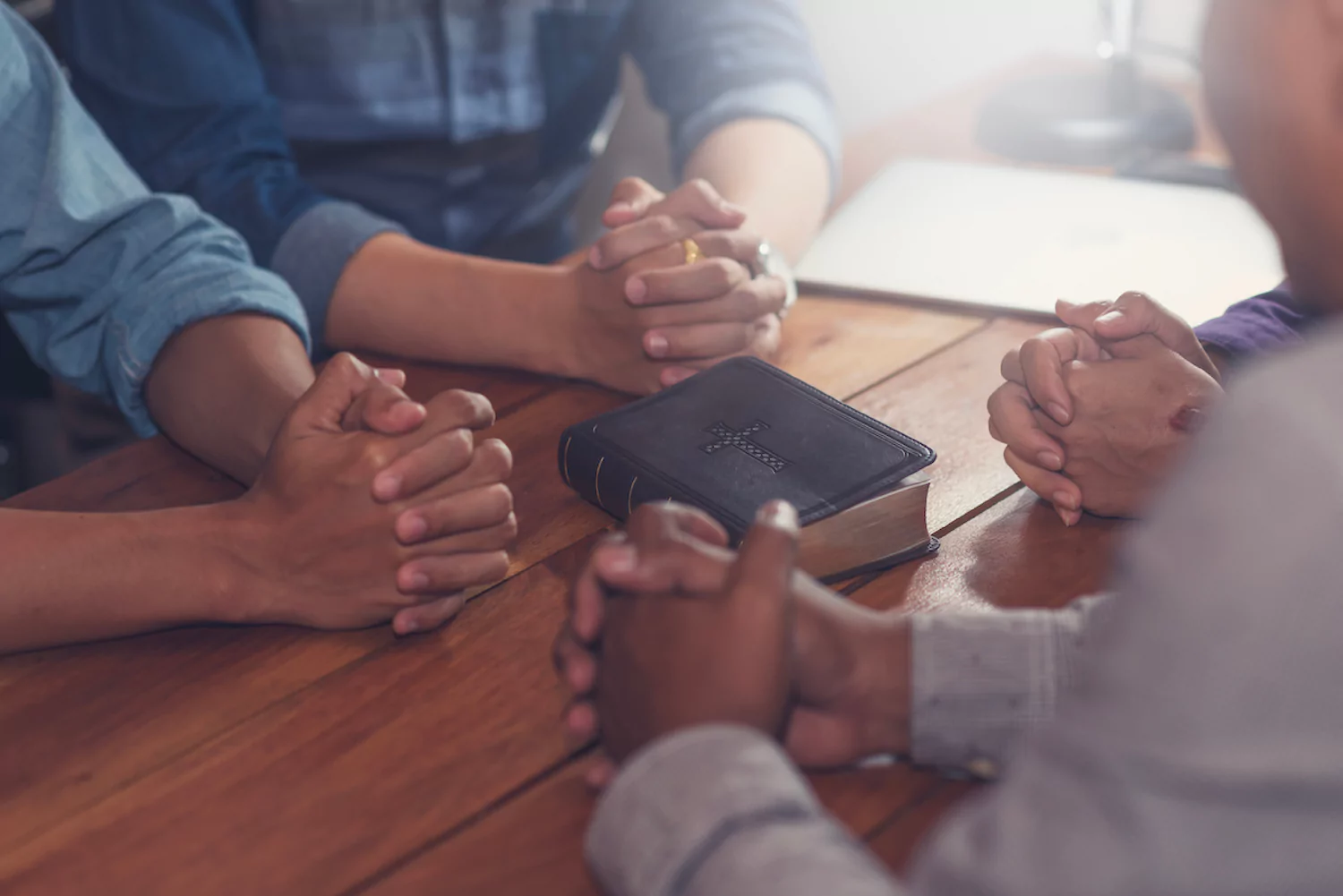 Four men sit at a table together with hands folded to pray.